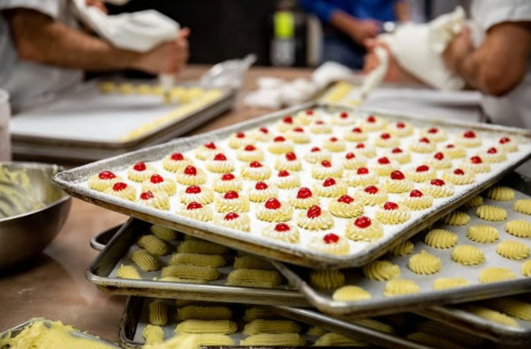 Trays of small frosted pastries with red toppings on a bakery worktable