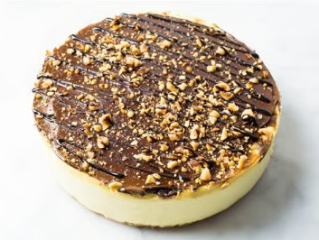 Round chocolate-topped dessert with chopped nuts on a white plate