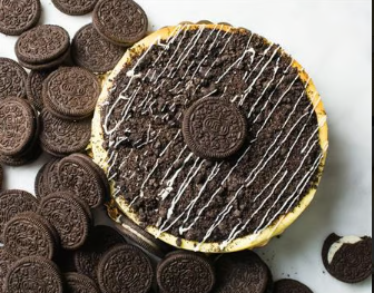 Chocolate dessert topped with Oreo cookies and white drizzle, surrounded by scattered Oreos