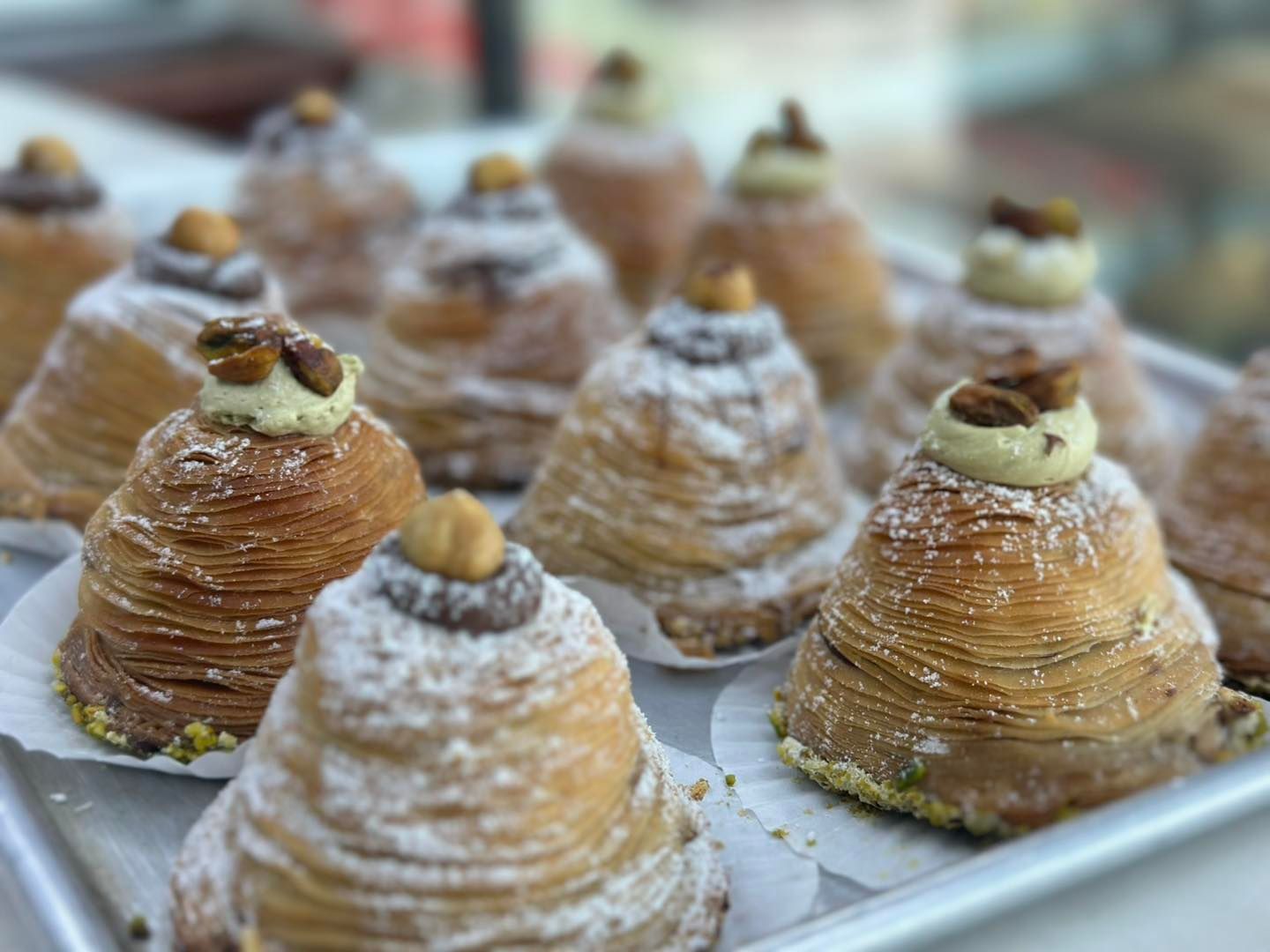 Tray of sugar-dusted cone-shaped pastries topped with nuts in a bakery display
