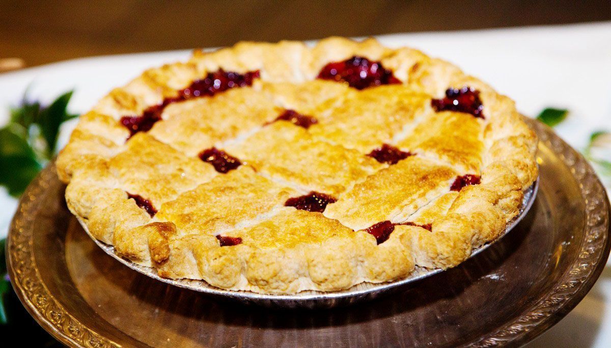 A golden-brown fruit pie with lattice crust and red filling on a plate