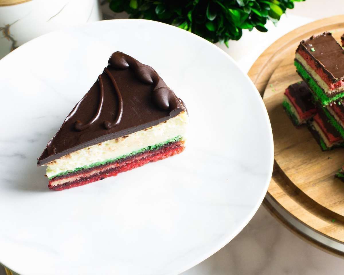 Chocolate-topped layered cake slice on a white plate beside another slice on a wooden board.