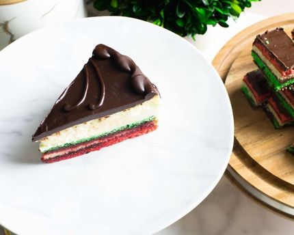 Chocolate-topped layered cake slice on a white plate beside another slice on a wooden board.