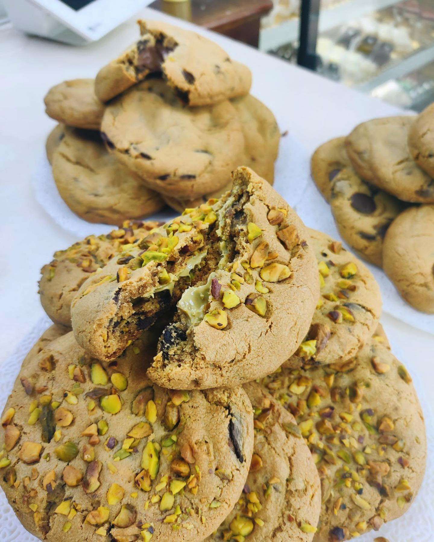Stacked pistachio cookies on a tray, with chocolate chunks and green nut pieces visible.