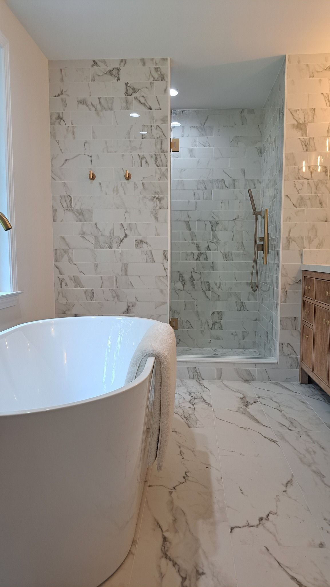 Bathroom with marble tile, free-standing white tub, and glass shower.