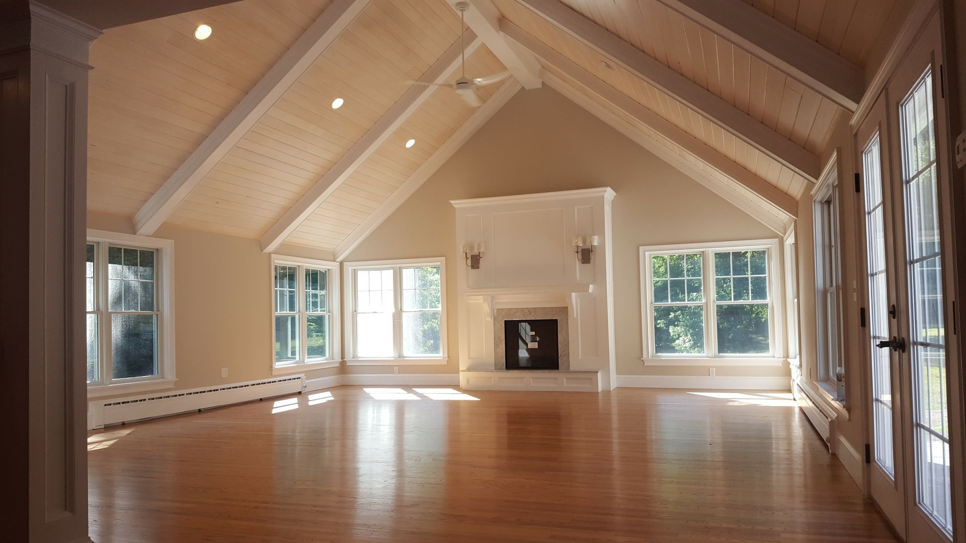Empty room with vaulted ceiling, fireplace, windows, and hardwood floors.
