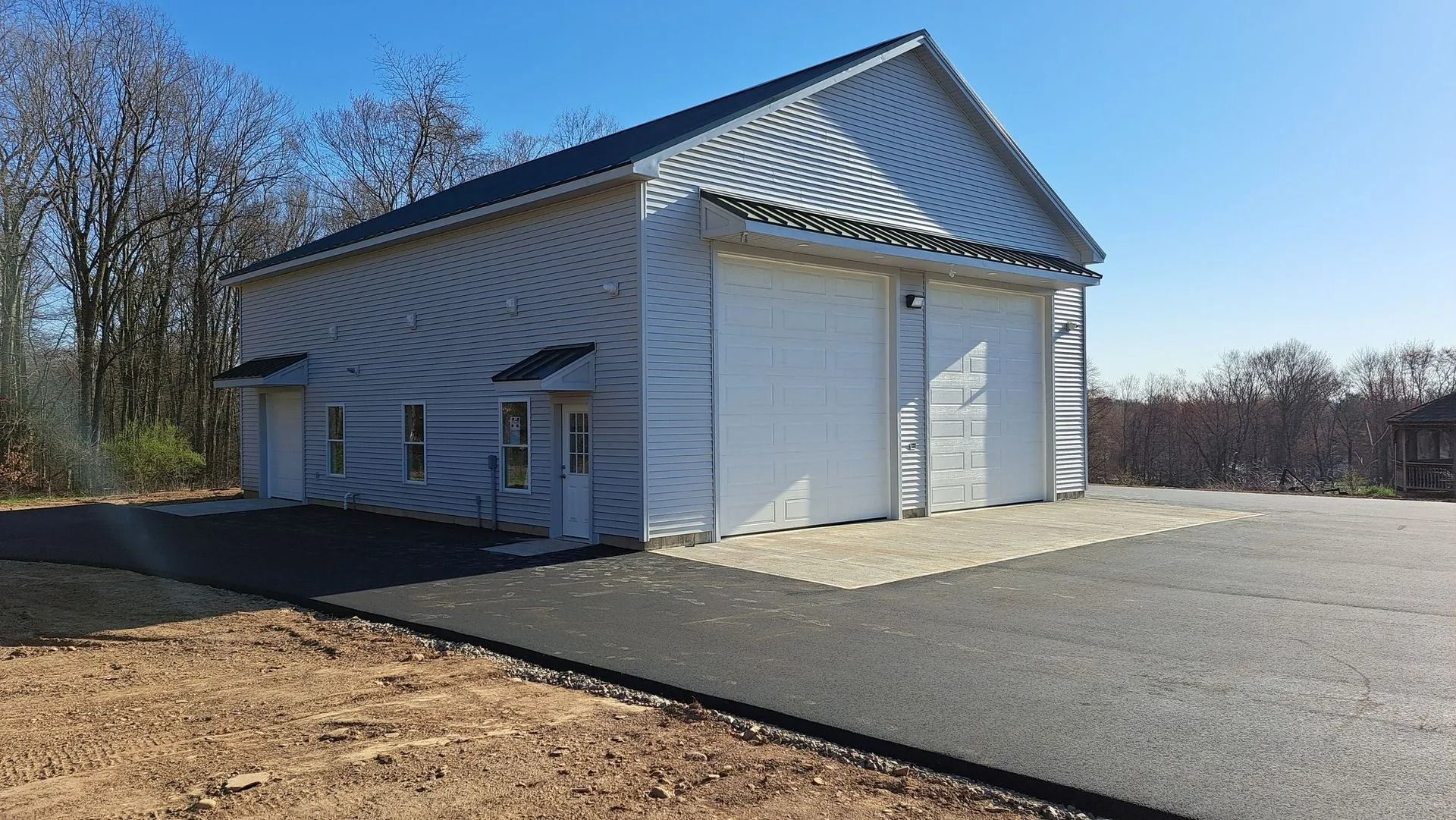 Metal garage building with two large garage doors, two small side doors, and asphalt driveway.