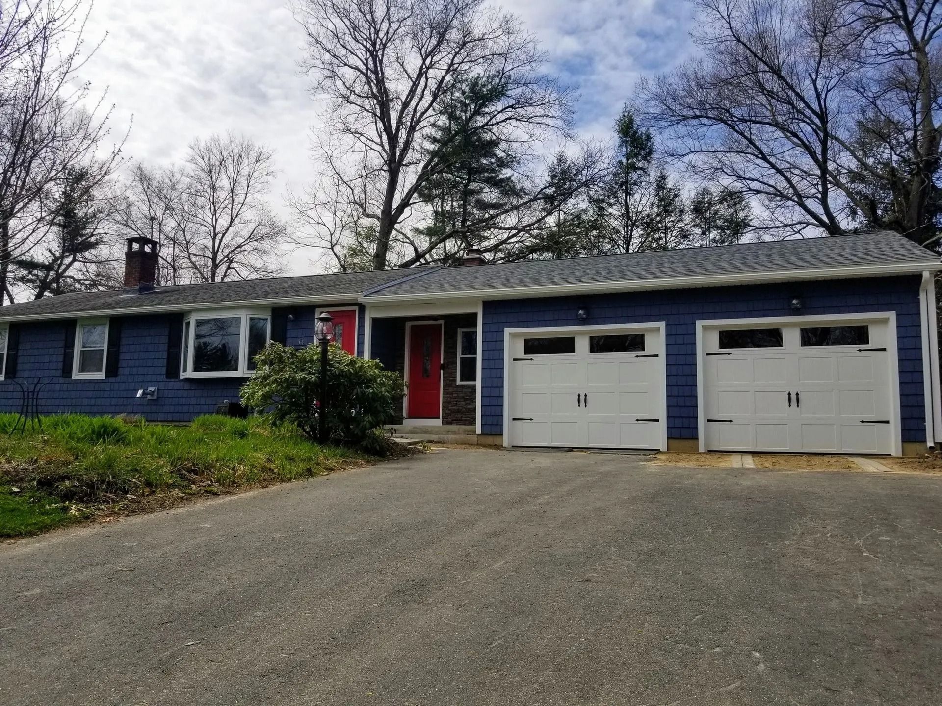 Blue ranch house with a two-car garage, red door, and asphalt driveway.