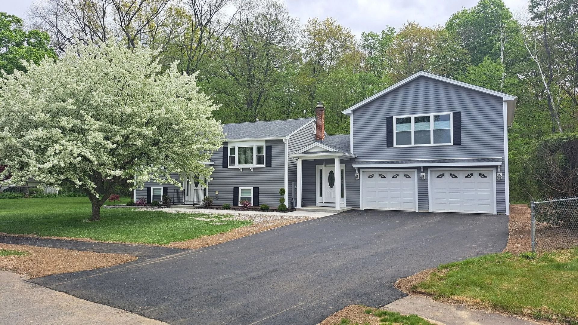 Gray house with black shutters, attached garage, and a flowering tree in the front yard.