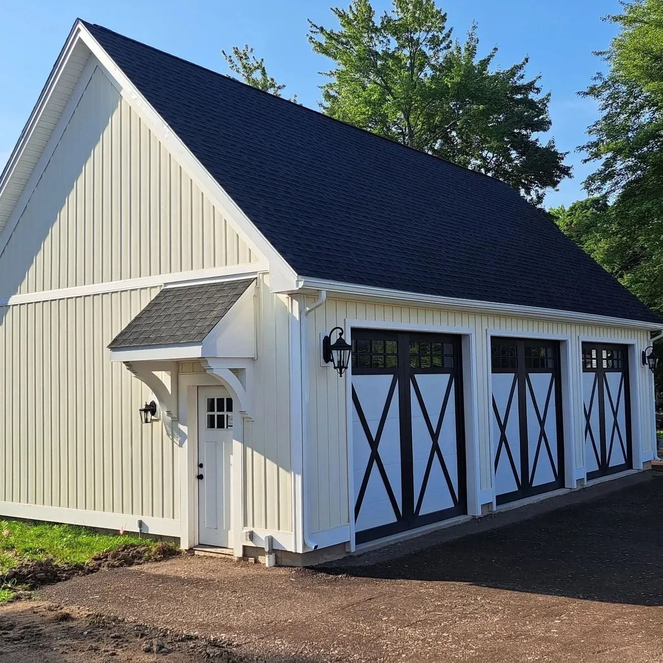 White barn-style garage with black doors and roof. Small entry door with an awning.