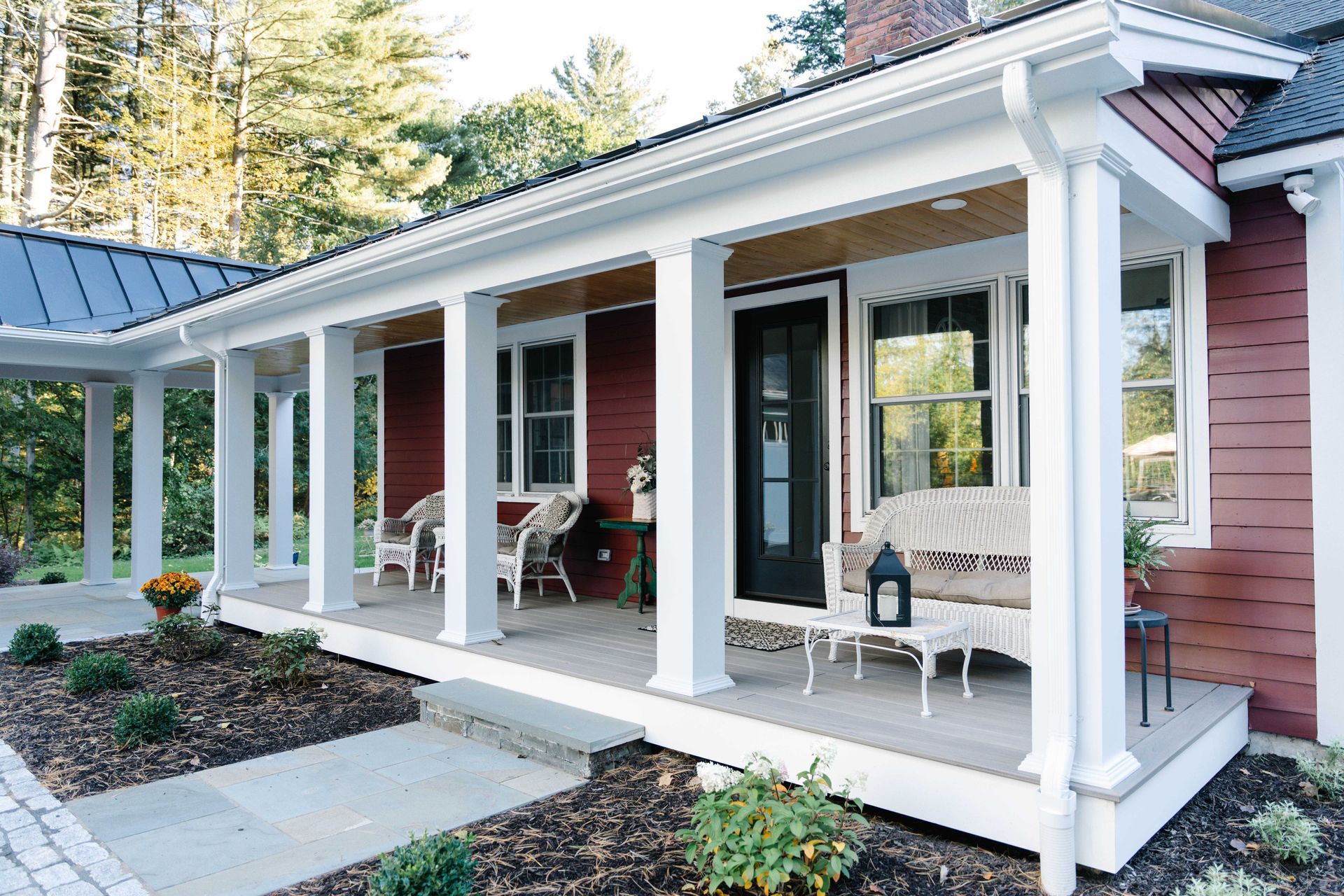 Red house with white columns, porch with seating, and a black front door.
