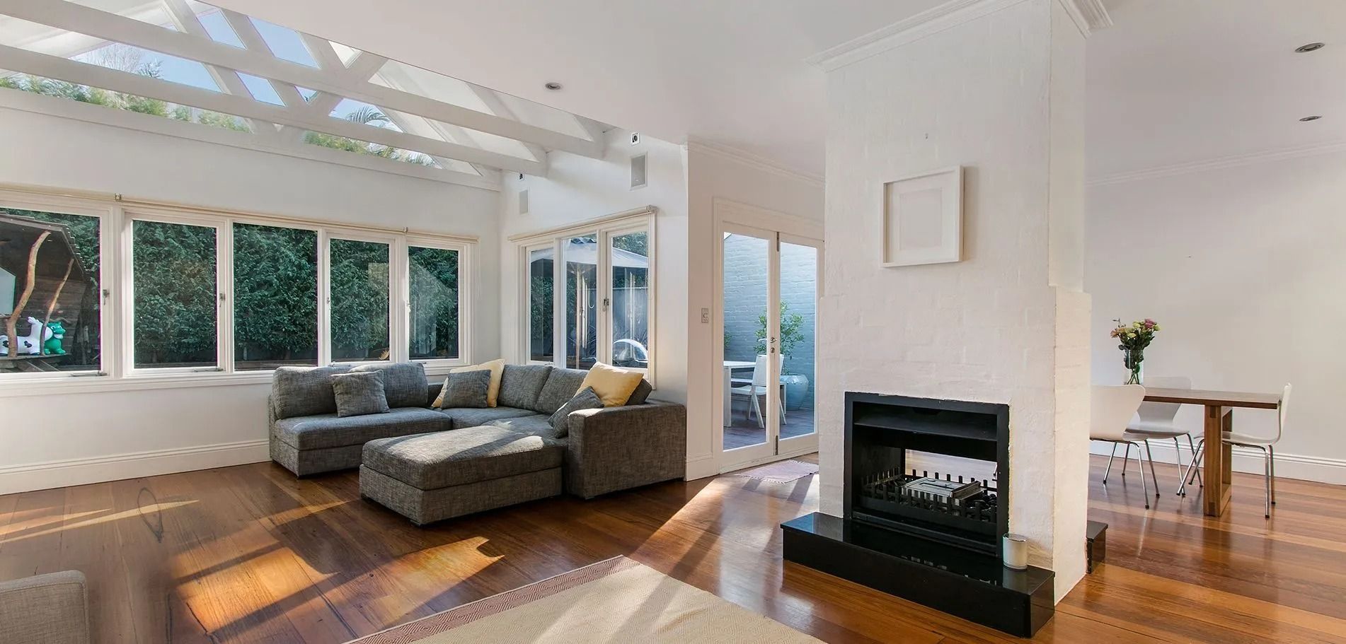 A bright living room with large windows, a gray sectional sofa, and a fireplace.