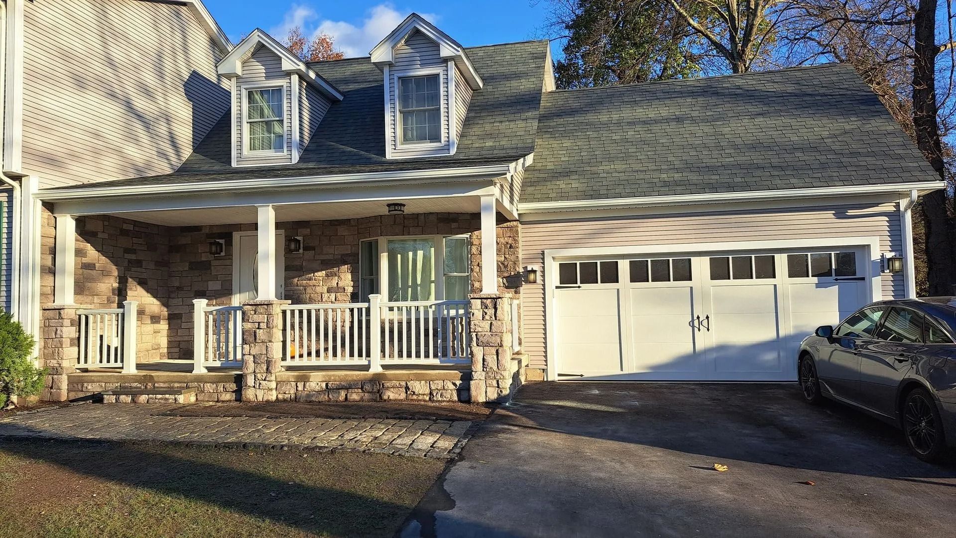 House with stone facade, porch, garage, and dormer windows on a sunny day.
