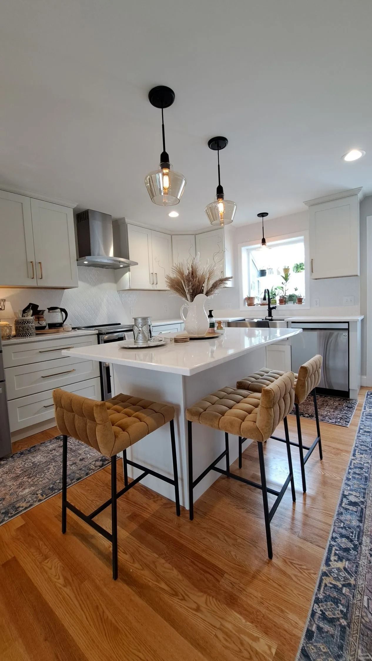 Modern kitchen with white cabinets, island, and pendant lights. Barstools and a rug add warmth.