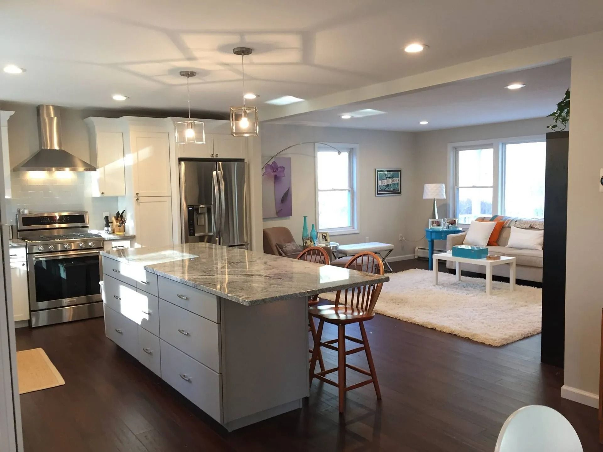 Open-concept kitchen and living room with white cabinetry, island, stainless steel appliances, and dark wood floors.