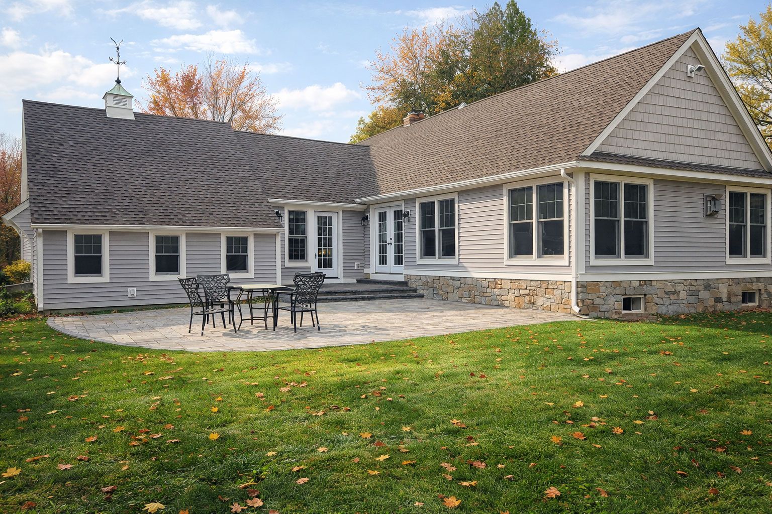 Backyard patio of a house with gray siding, stone foundation, and a small table and chairs.