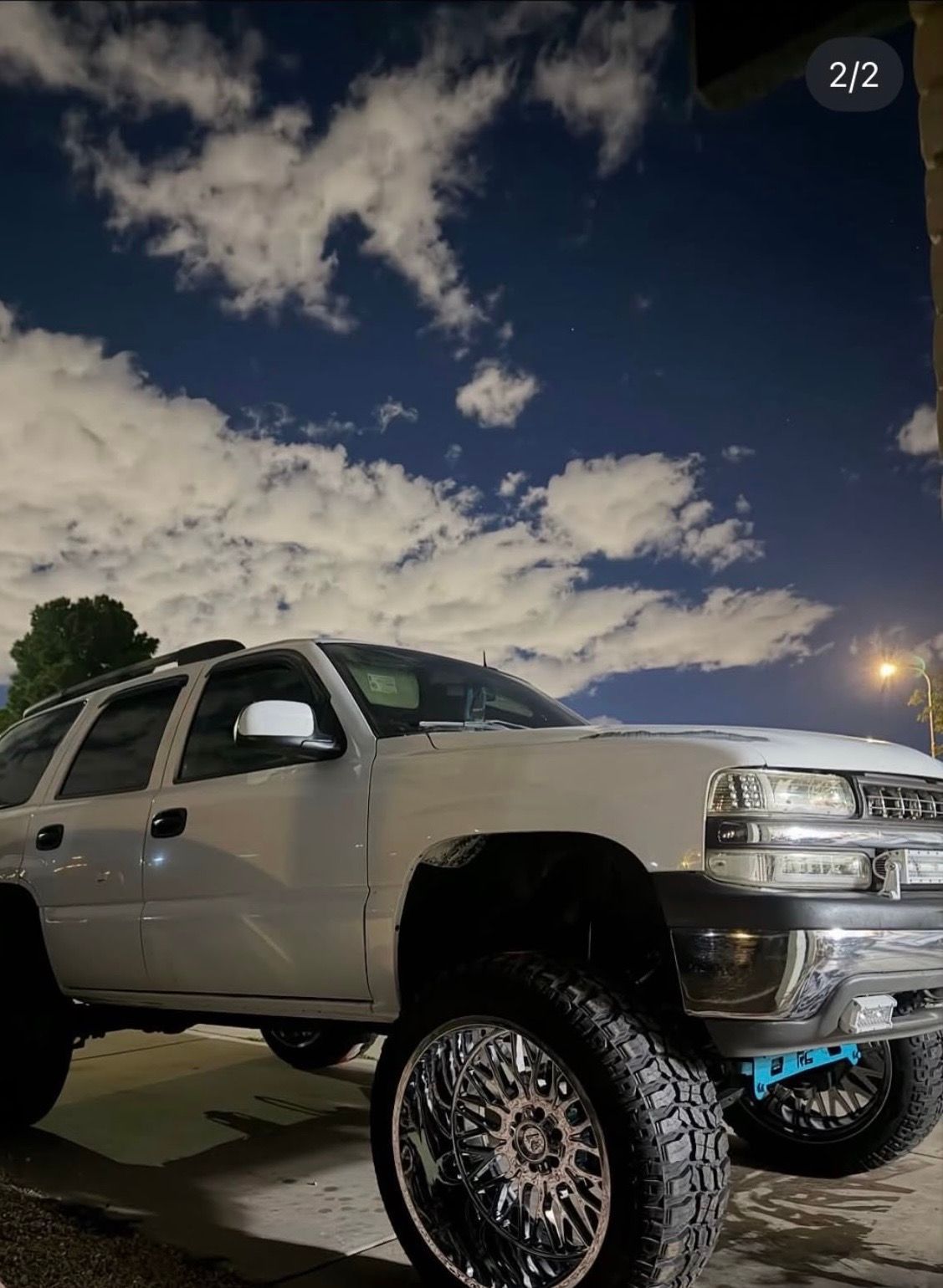 Lifted white SUV with oversized chrome wheels parked outdoors at dusk under a cloudy sky.