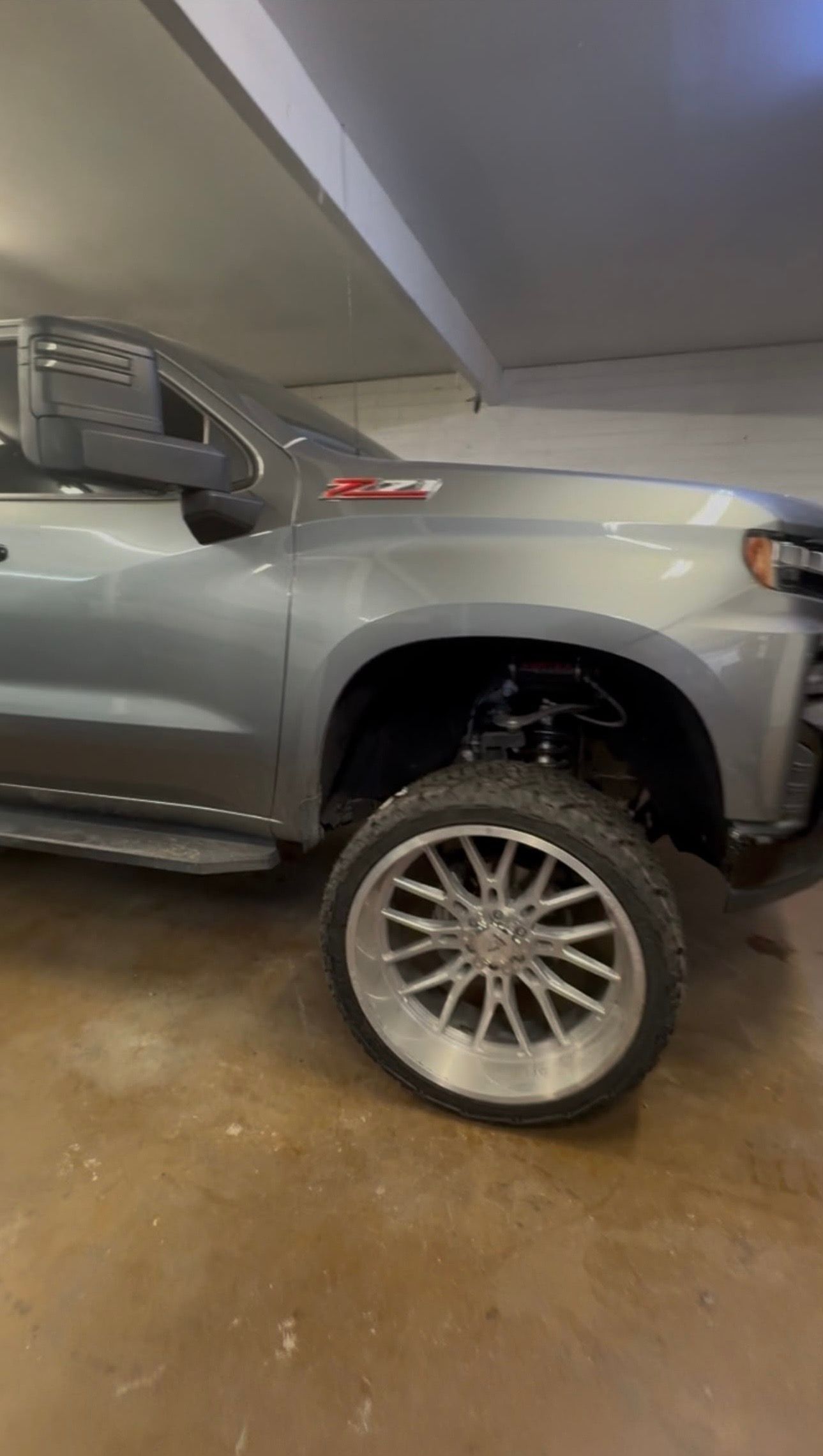 Silver pickup truck parked in a garage, front wheel removed and resting beside it.
