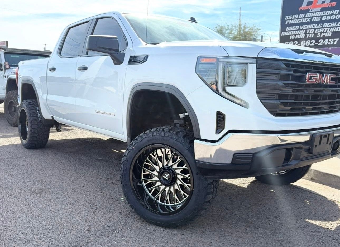 White GMC lifted pickup truck with black wheels parked outdoors at a dealership.