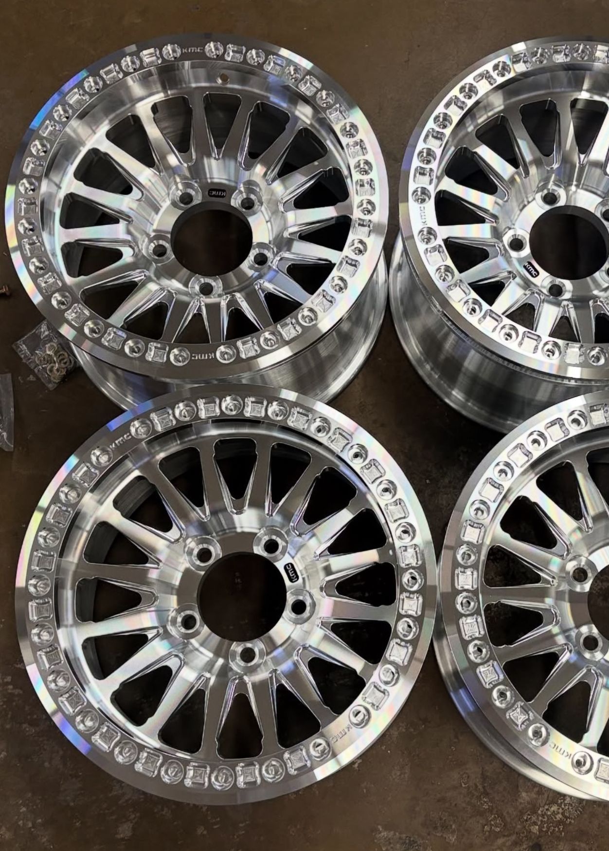 Four chrome alloy wheels with rhinestone trim arranged in a square on a dark surface.