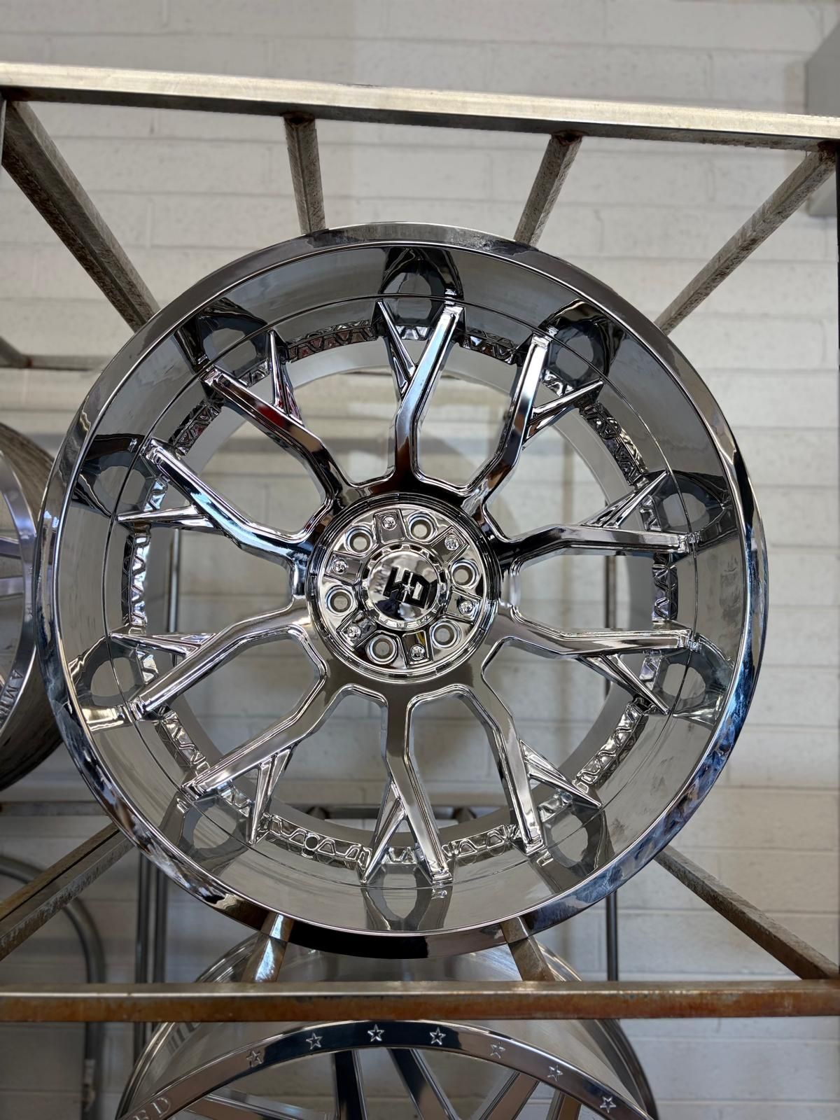 Chrome multi-spoke custom car wheel mounted on a wooden display rack.