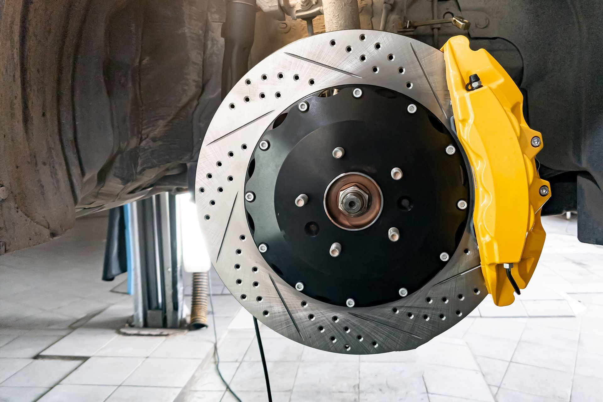 Close-up of a car brake disc and yellow caliper on a vehicle wheel assembly.