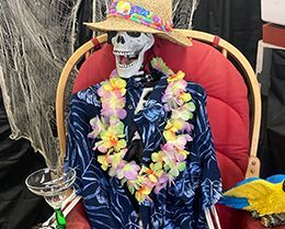 A skeleton is sitting in a chair wearing a shirt and hat