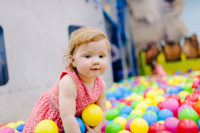 Toddler in a pink dress leaning among colorful plastic balls in a play area