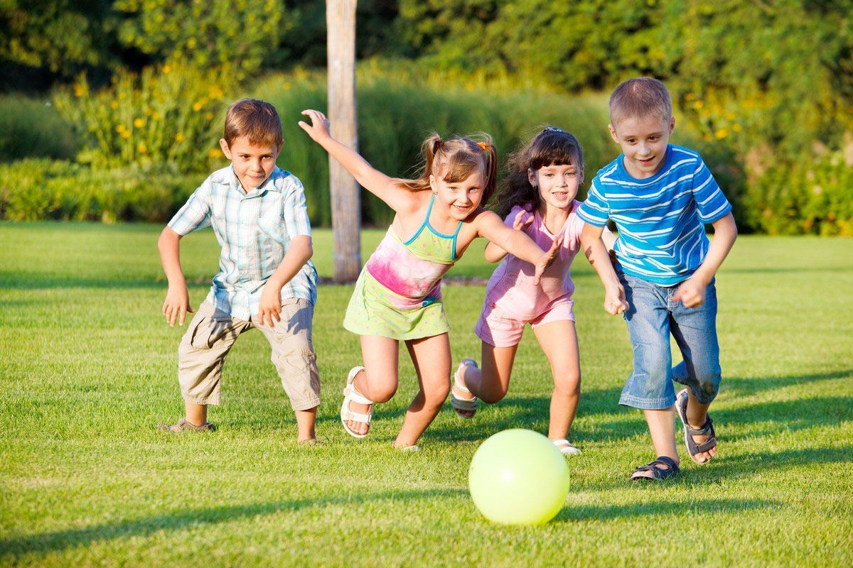 Children running toward a bright ball on a grassy field outdoors
