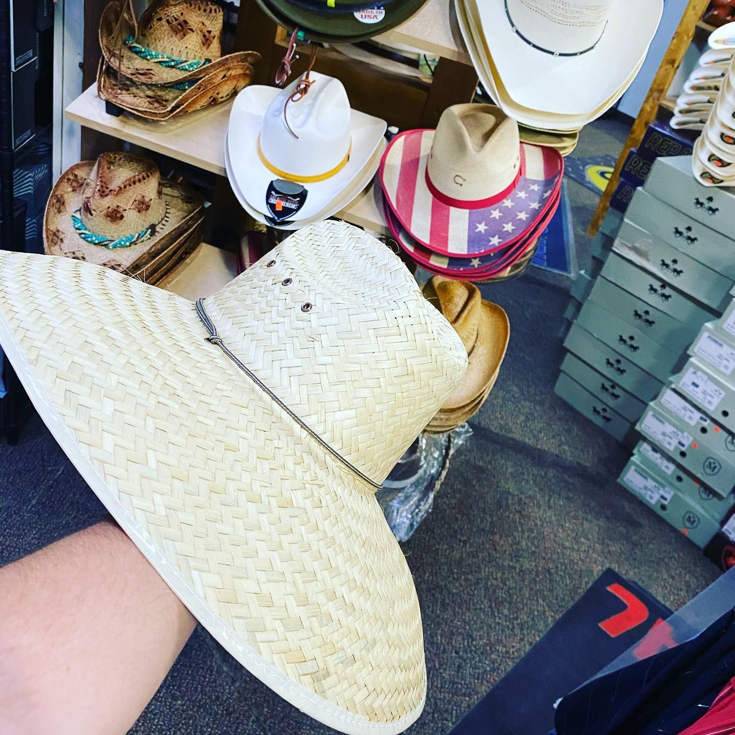 A person is holding a straw hat in front of a display of cowboy hats