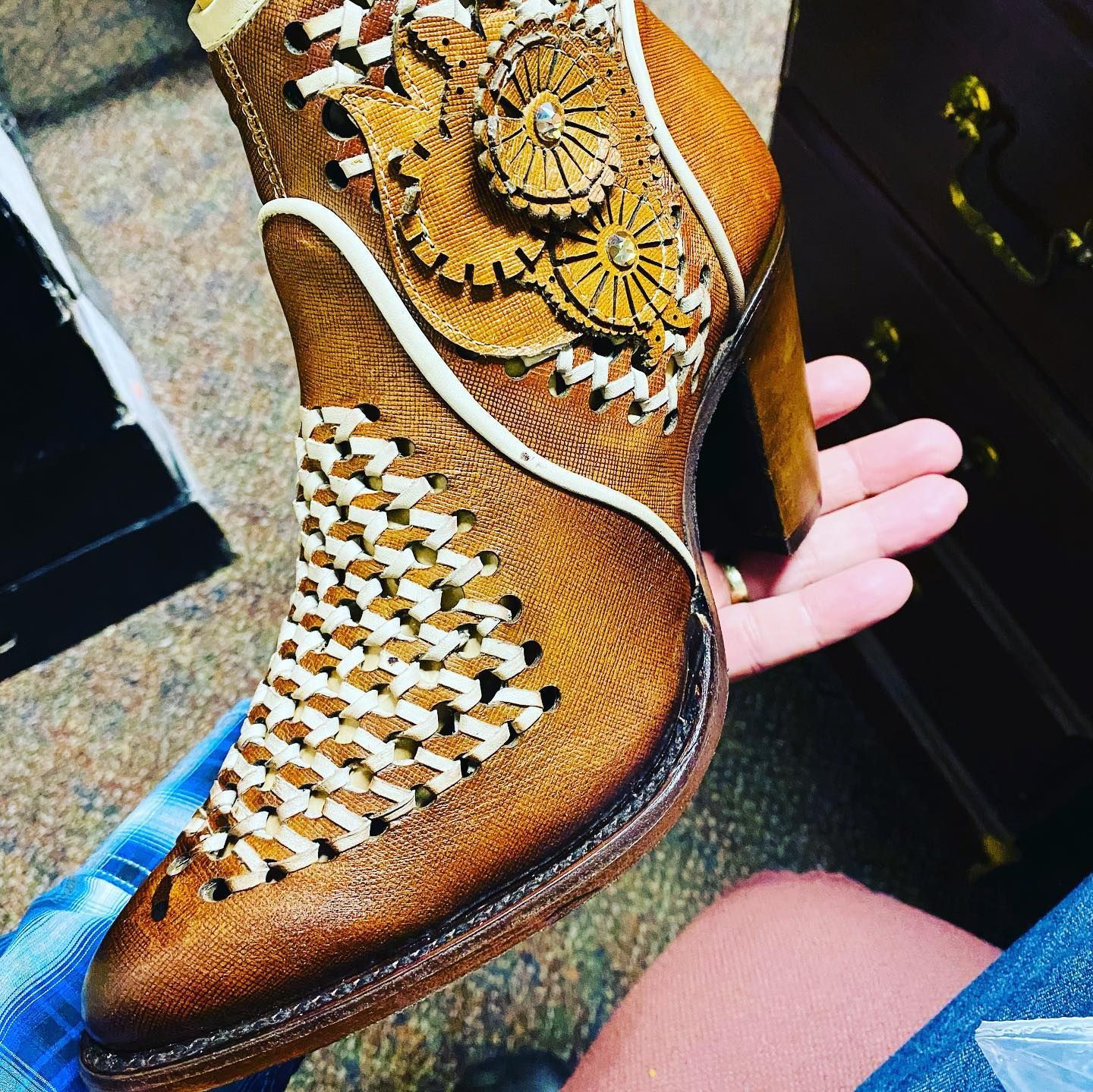 A person is holding a pair of brown cowboy boots