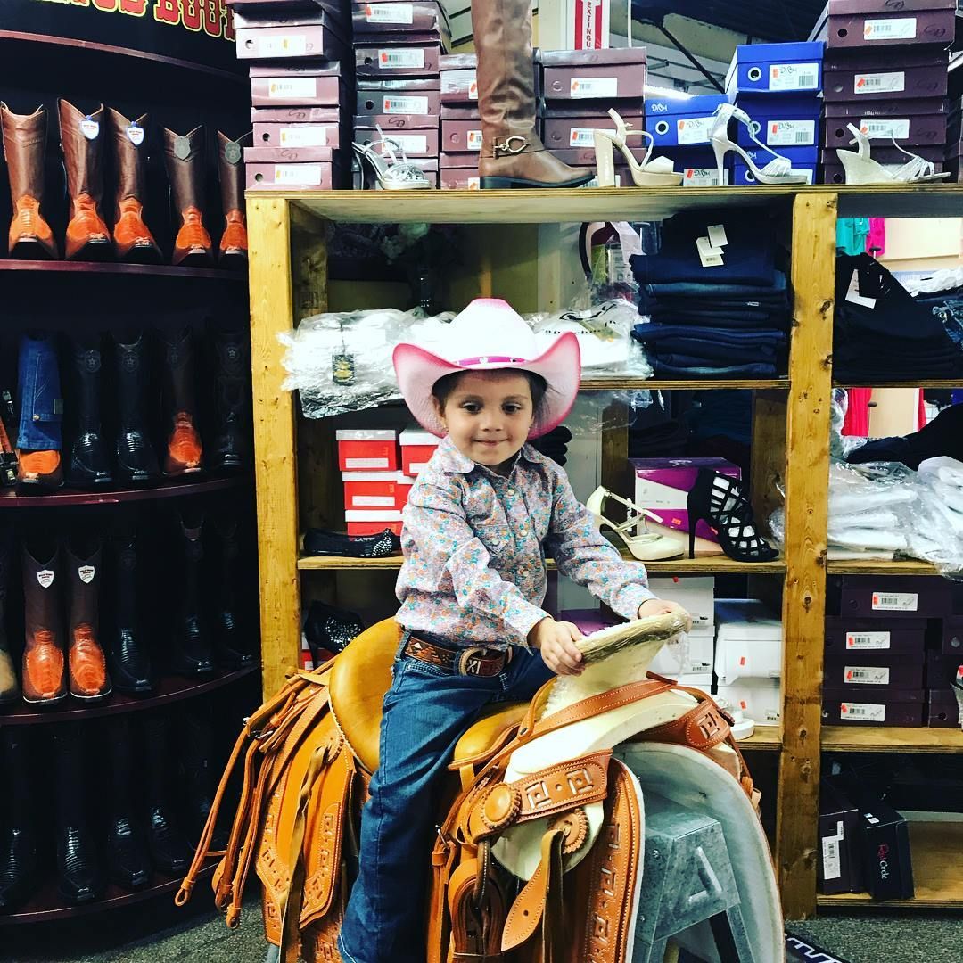 A little boy in a cowboy hat is sitting on a saddle in a store.