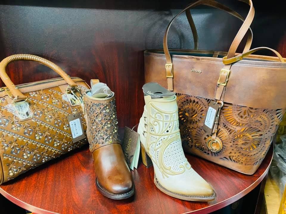 A pair of cowboy boots and a purse are on a wooden table.