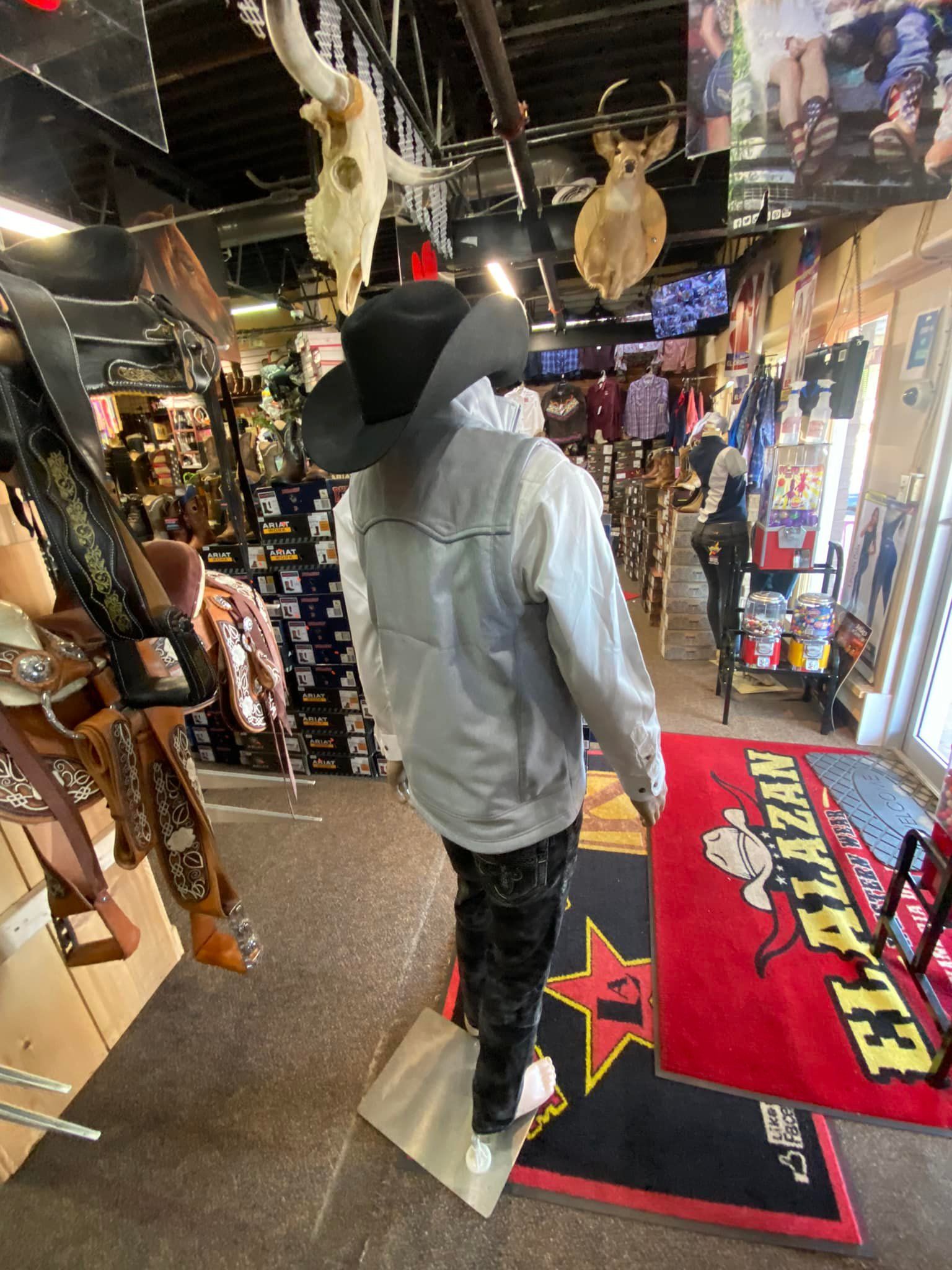 A man in a cowboy hat is standing on a mannequin in a store.