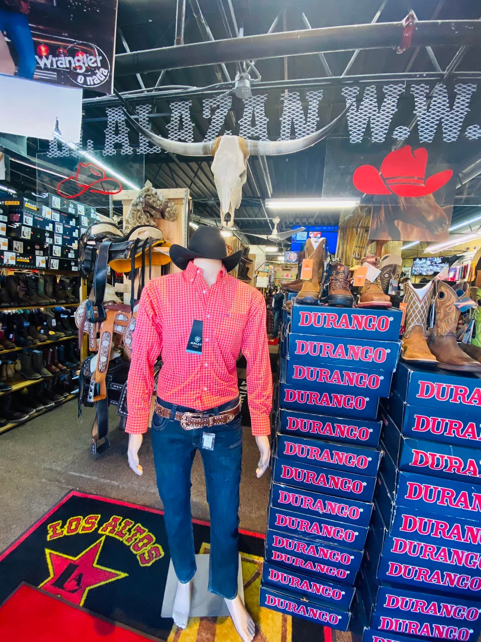 A mannequin is wearing a pink shirt and a cowboy hat in a store.