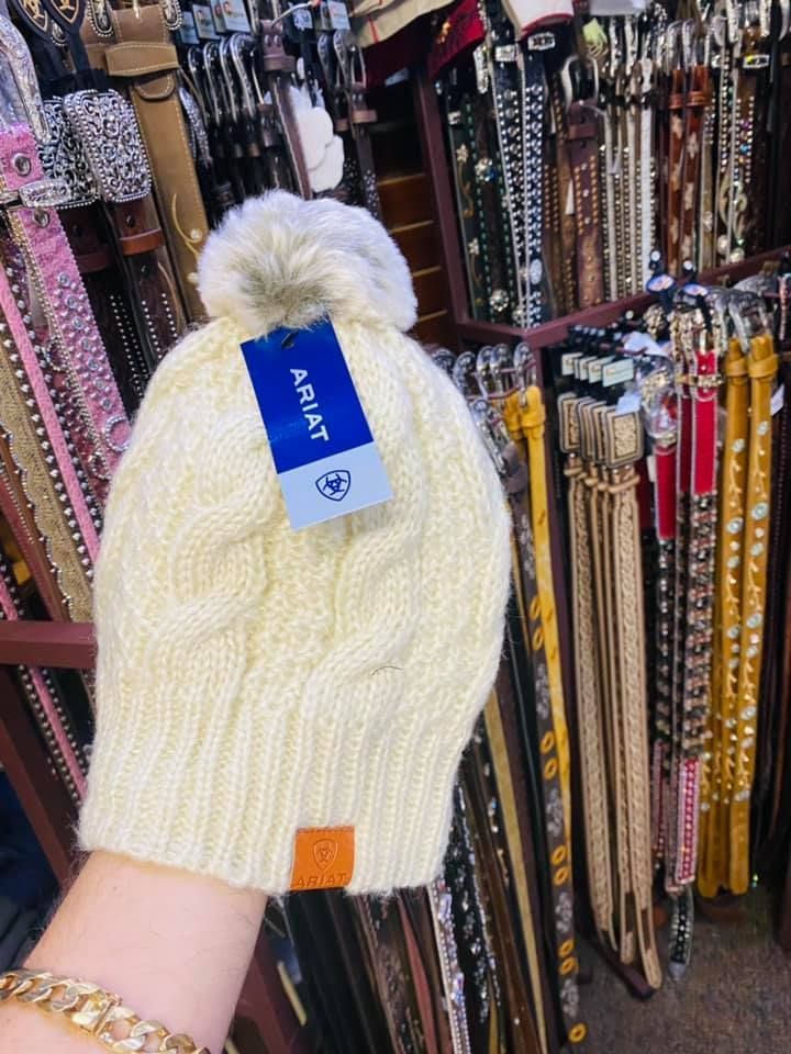 A person is holding a white knitted hat in front of a shelf of belts.