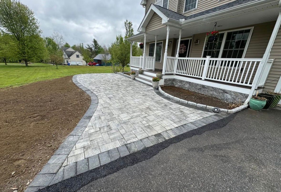 Curved stone walkway beside a white porch and driveway, with a small landscaped mulch bed.