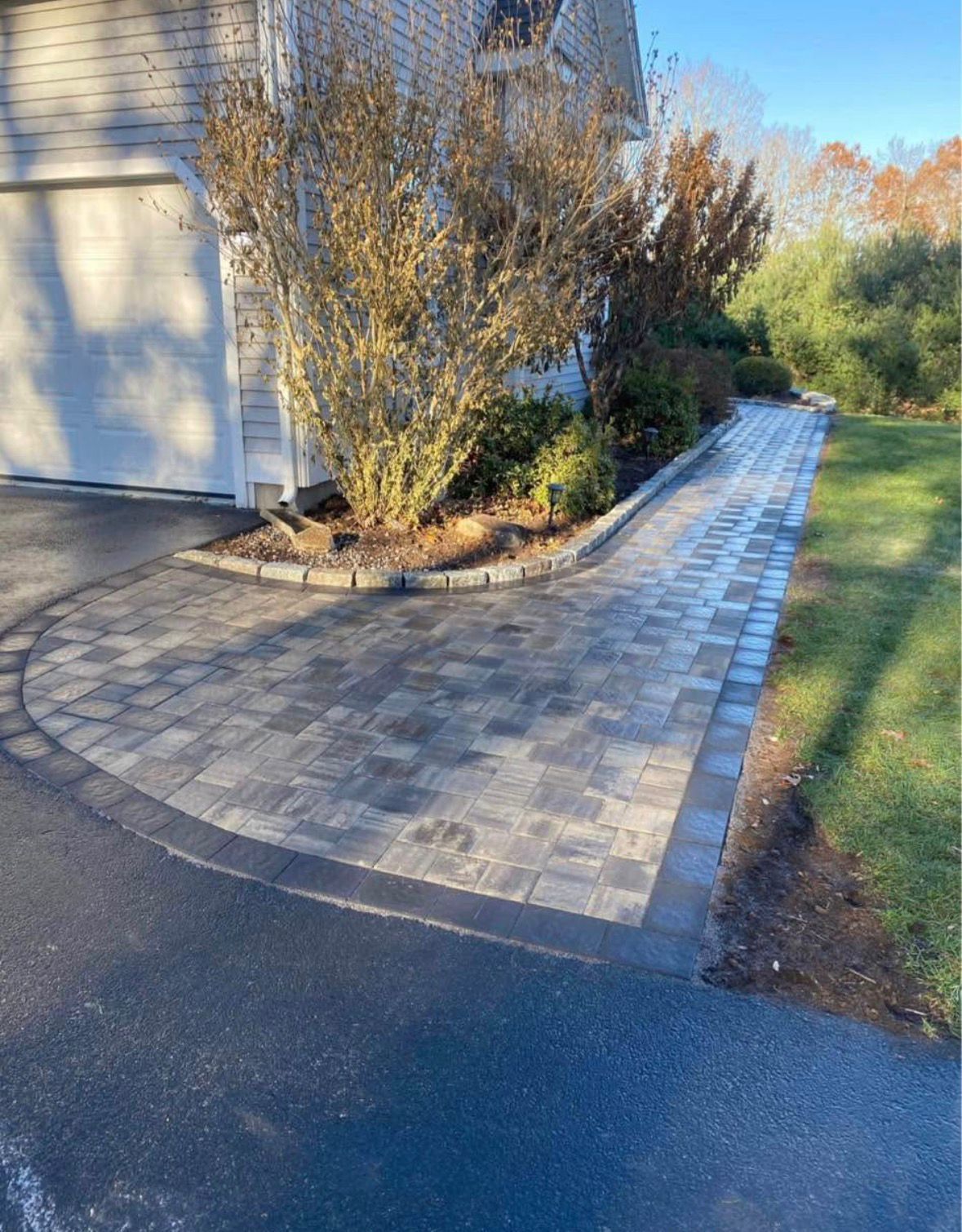 Paved walkway along a house beside shrubs and a lawn in autumn light