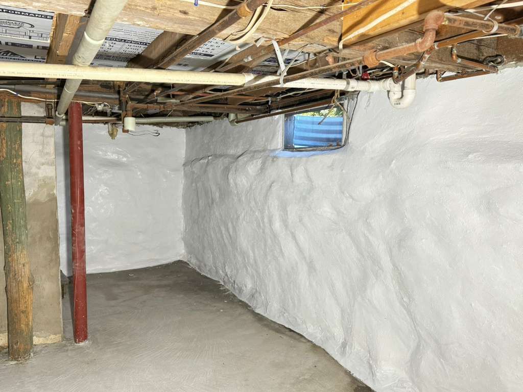 Unfinished basement crawlspace with white insulated walls, exposed pipes and joists, and a small blue window.