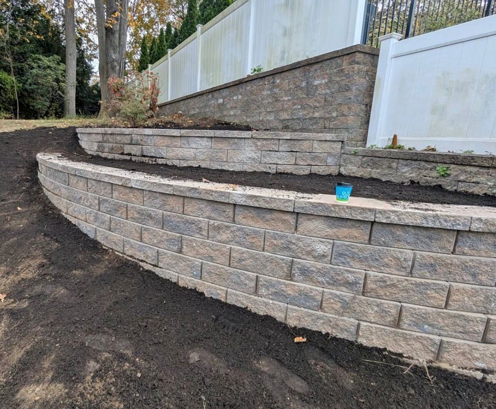 Stone retaining wall with curved steps beside a white fence and dirt landscaping