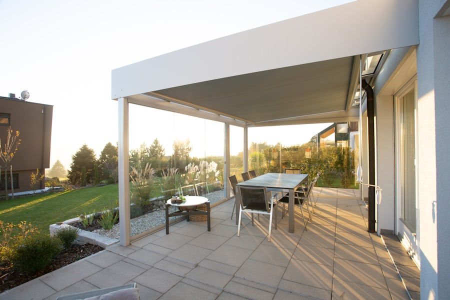 Modern patio with dining table, chairs, and shaded pergola beside a house at sunset