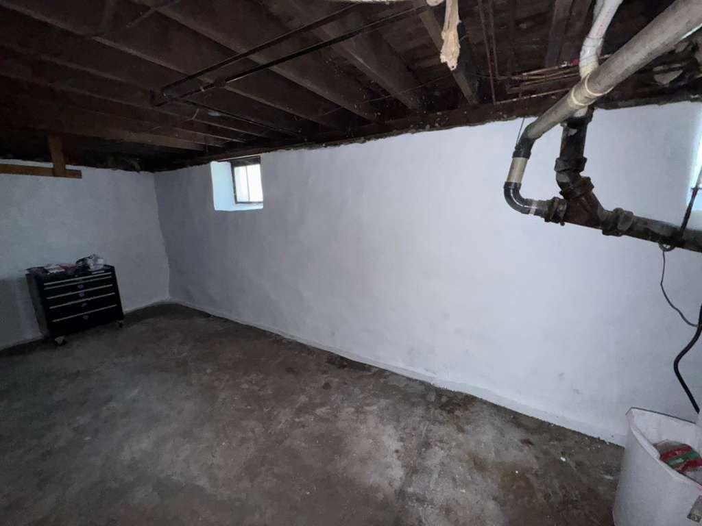 Empty basement room with concrete floor, white walls, exposed ceiling beams, and a small window.