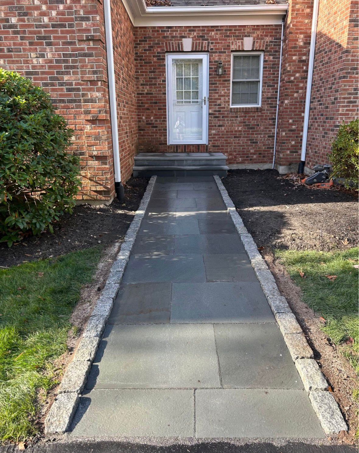 Brick house entry walkway with concrete path leading to a white front door.