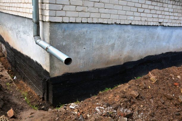 Exterior foundation with black waterproofing and a gray drain pipe on a brick house corner
