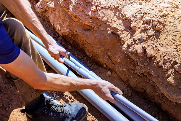 Person laying black pipes in a dirt trench