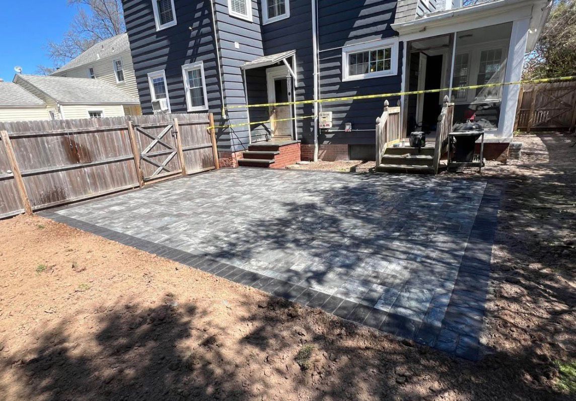 Backyard patio with newly laid paver seating area beside a dark blue house and wooden fence