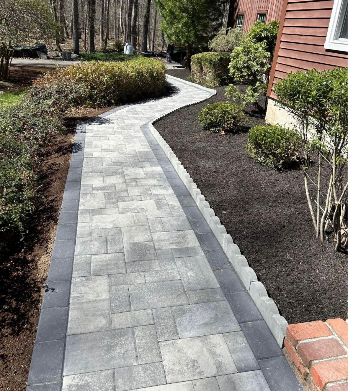 Curved gray paver walkway through a landscaped yard beside a house