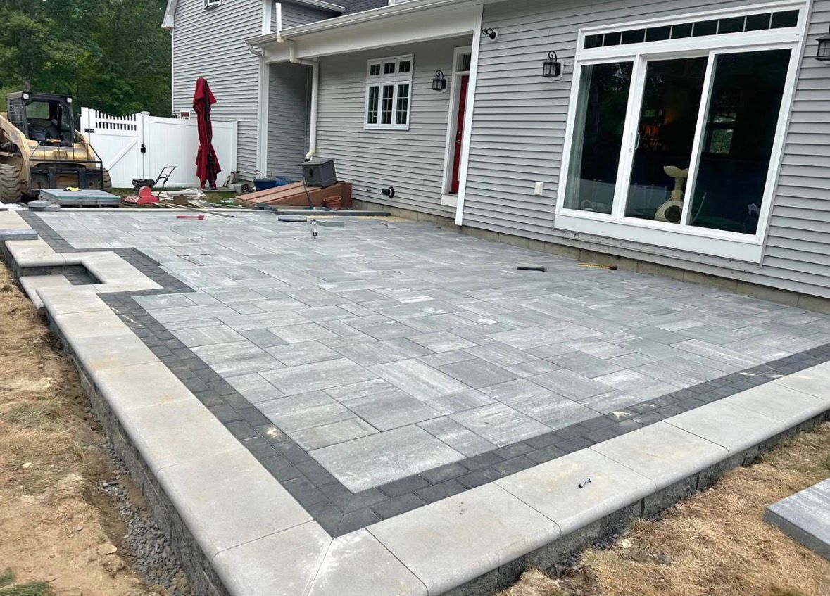 Freshly paved gray stone patio beside a house with large sliding glass doors and a concrete border