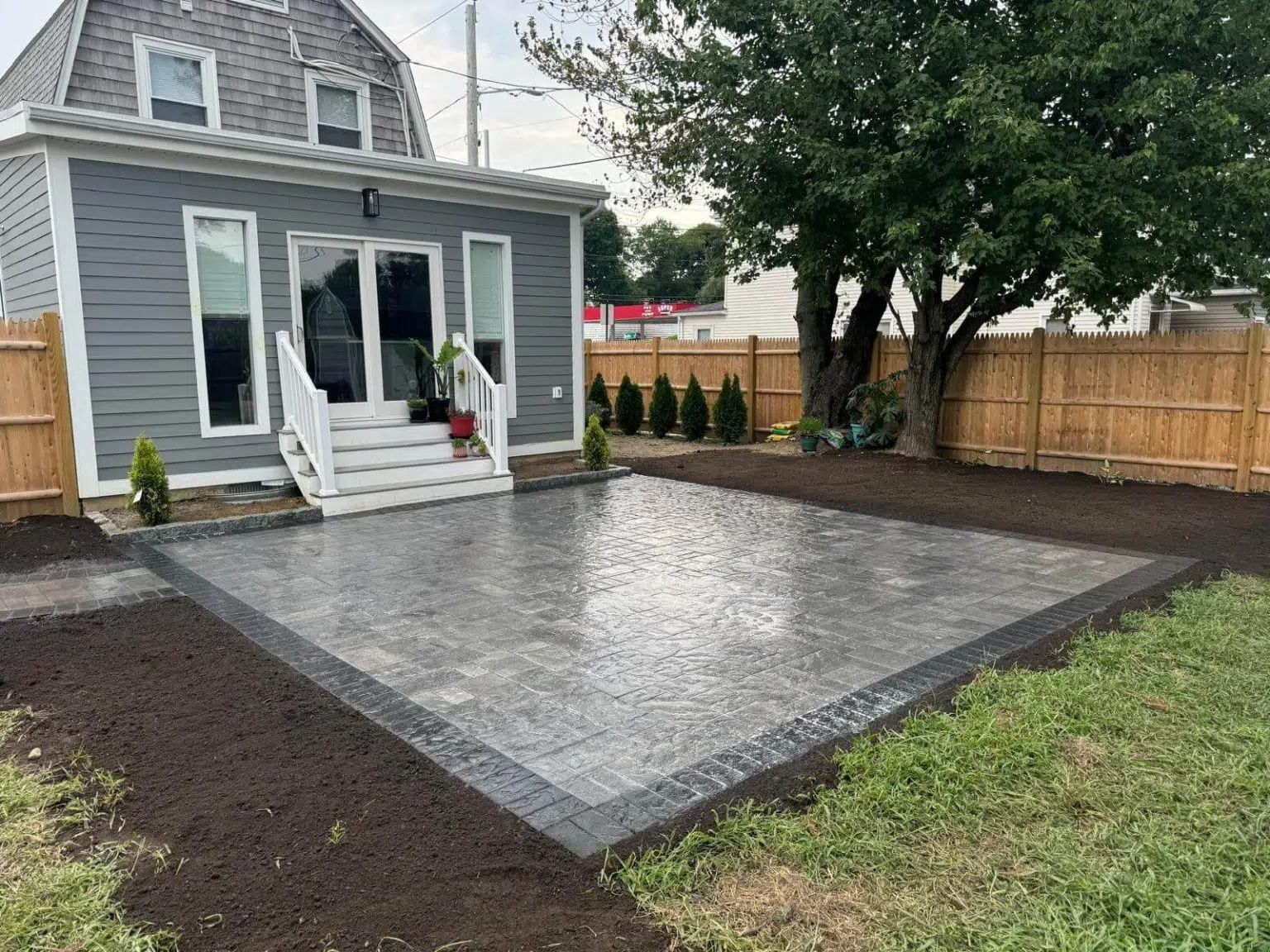 Backyard patio with a gray paver surface beside a gray house and white steps.