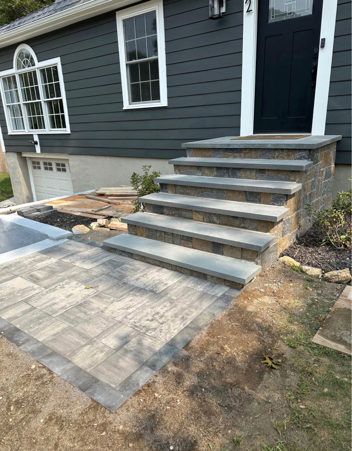 Front steps leading to a dark gray house with a paved walkway and small front yard.